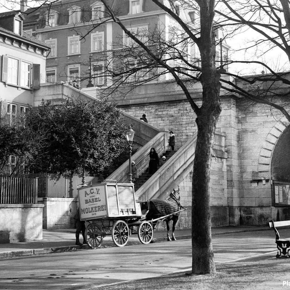 Milchwagen der ACV Basel Molkerei mit Pferd unter einer steinernen Treppe und Brücke in Basel, mit Gaslaterne und kahlem Baum