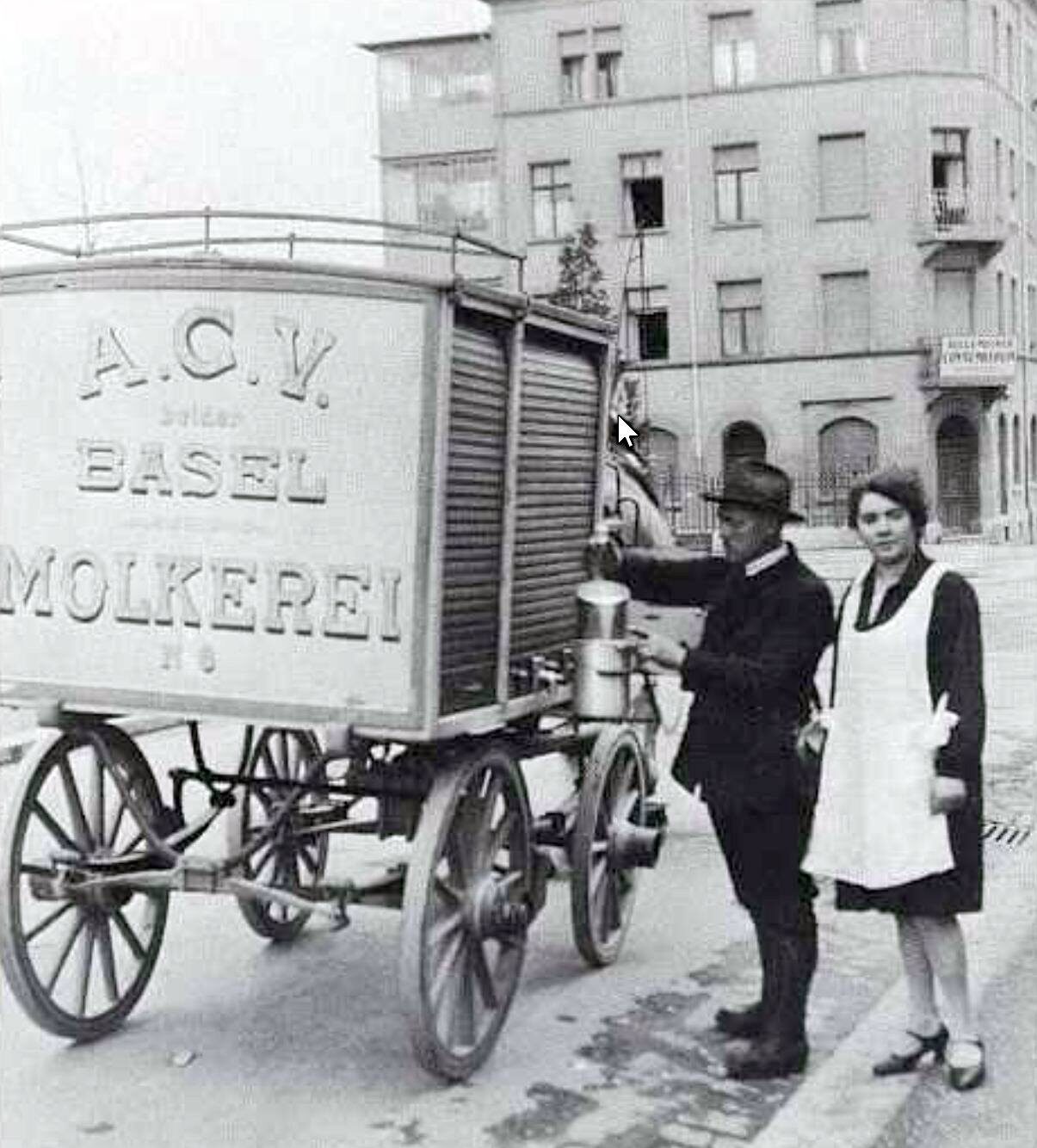 Milchmann der ACV Basel Molkerei und eine Kundin mit weisser Schürze und Milchkanne an einer Basler Strassenecke