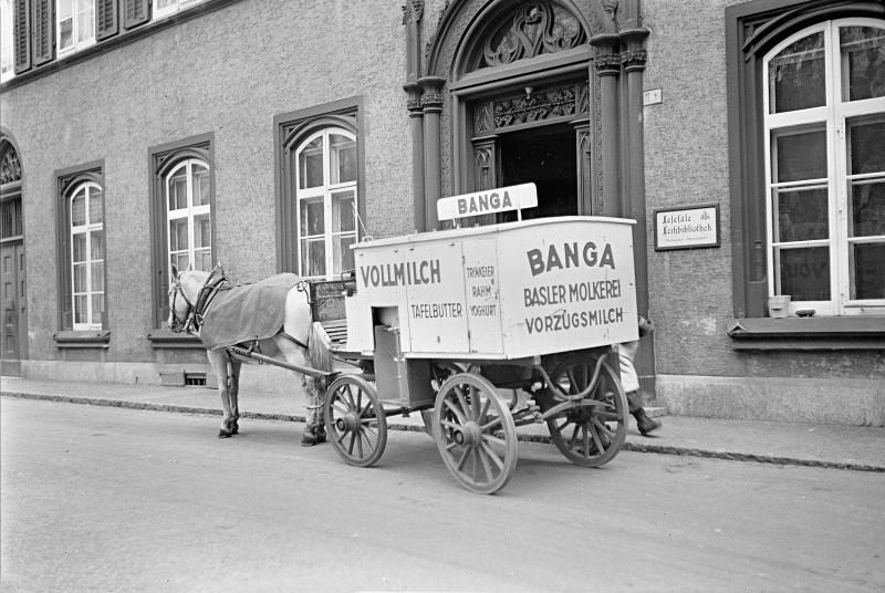 Pferdebespannter Milchwagen der BANGA Basler Molkerei mit Werbung für Vollmilch, Tafelbutter, Trinkeier, Rahm und Yoghurt vor einem Basler Hauseingang